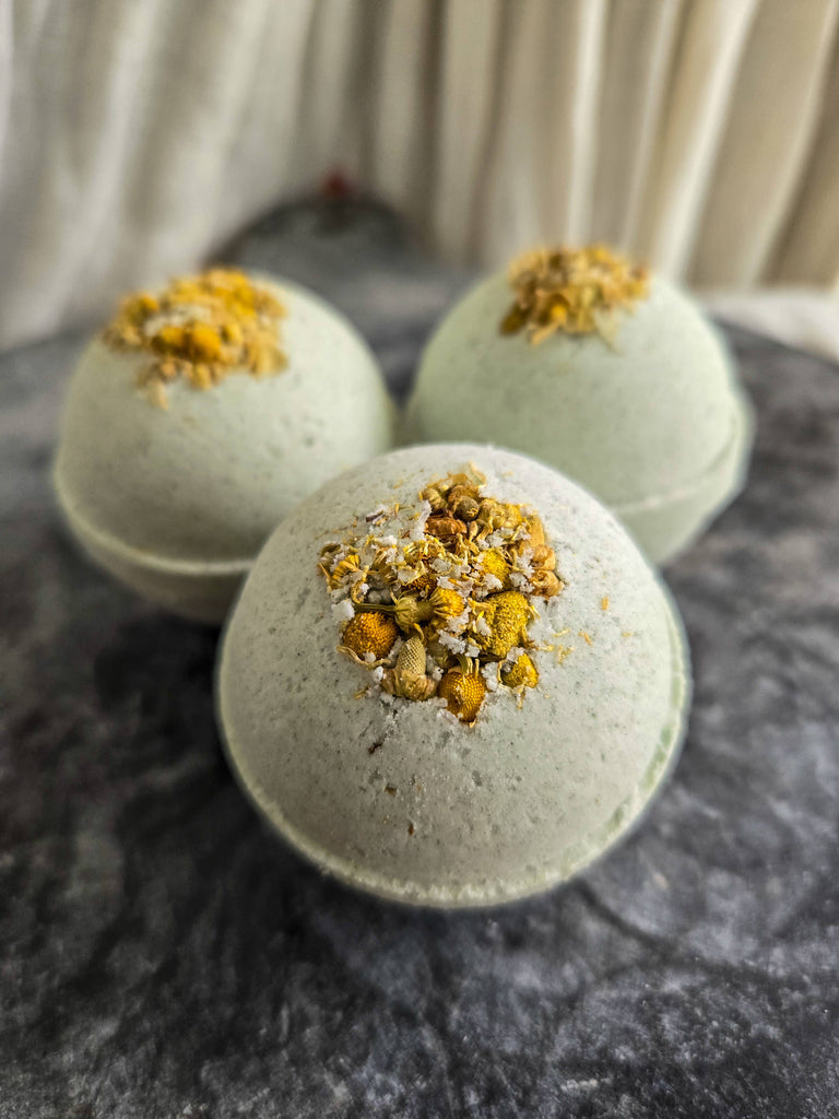 Refresh | Natural Bath Bomb by Gnat and Bee: three pale green fizzies topped with dried yellow and white flowers are displayed on a gray surface, ideal for those seeking gentle respiratory support during bath time.