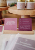 A wooden stand displays two JaxKelly Shower Affirmation™ Cards - Boundaries, including Not every thought that enters my mind deserves my attention. Gold-lidded jars and more affirmation cards appear in the background.