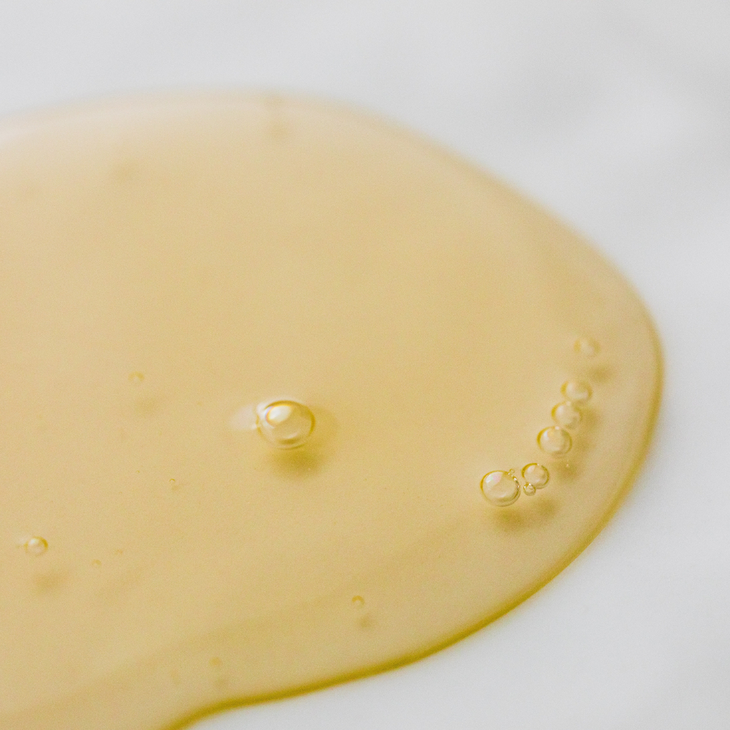 A close-up of Bath Alliance Body Wash: CITRUS MINT / AMBER 8 OZ, a golden liquid with tiny bubbles, evokes the fresh scent of citrus on a white background.