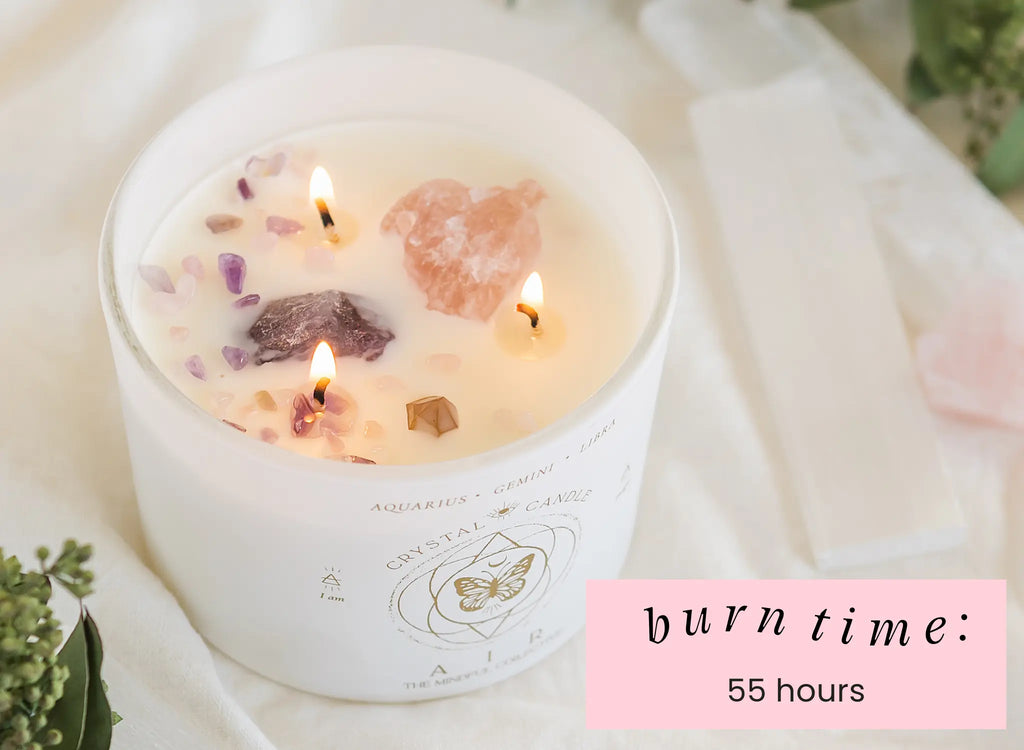 The Air Elements Candle 12oz by THE MINDFUL COLLECTIVE features crystals in white wax with three flames. Burn time: 55 hours. Greenery and crystals surround this unique Zodiac Candle.
