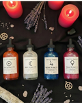 Four bottles of ritual oils with labels on a dark background with candles and lavender.