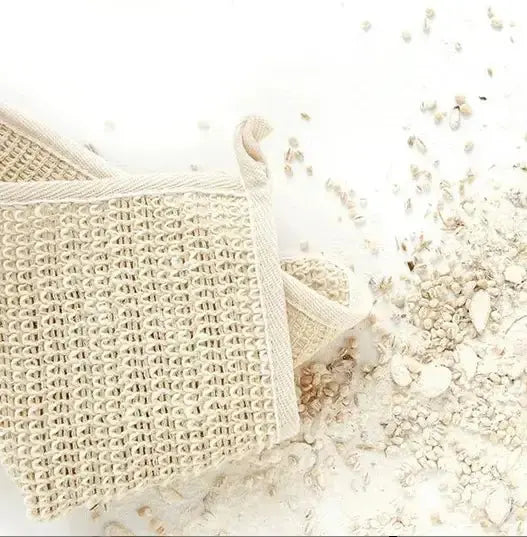 The beige Agave Wash Cloth by Nash and Jones rests on a white surface beside scattered oats, offering gentle exfoliation for your daily routine.