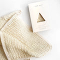 A cream-colored, textured Nash and Jones Agave Wash Cloth is displayed beside its packaging, which features a triangular cutout revealing the Natural Agave Wash Cloth inside.