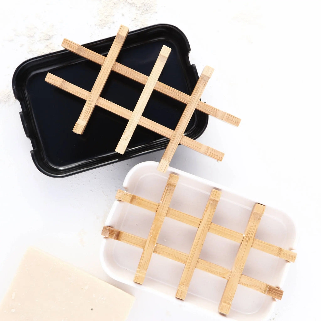 The Nash and Jones Bamboo Soap Dishes: Black are eco-friendly rectangular bamboo dishes, shown on a white surface with soap residue and a beige bar of soap nearby. Their bamboo grids add both style and sustainability.