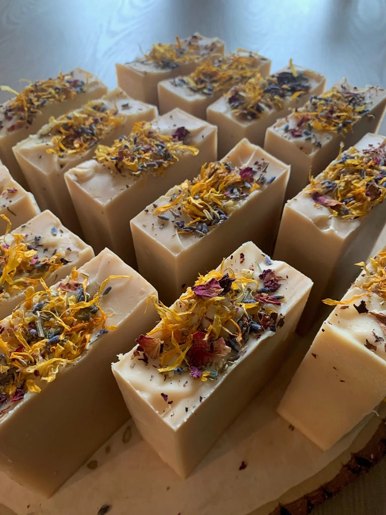 Several Bealtaine Sabbat Bars by Luna & Co. Soapery are arranged together, each rectangular bar adorned with yellow, purple, and red dried flower petals that highlight the beauty of their natural ingredients.