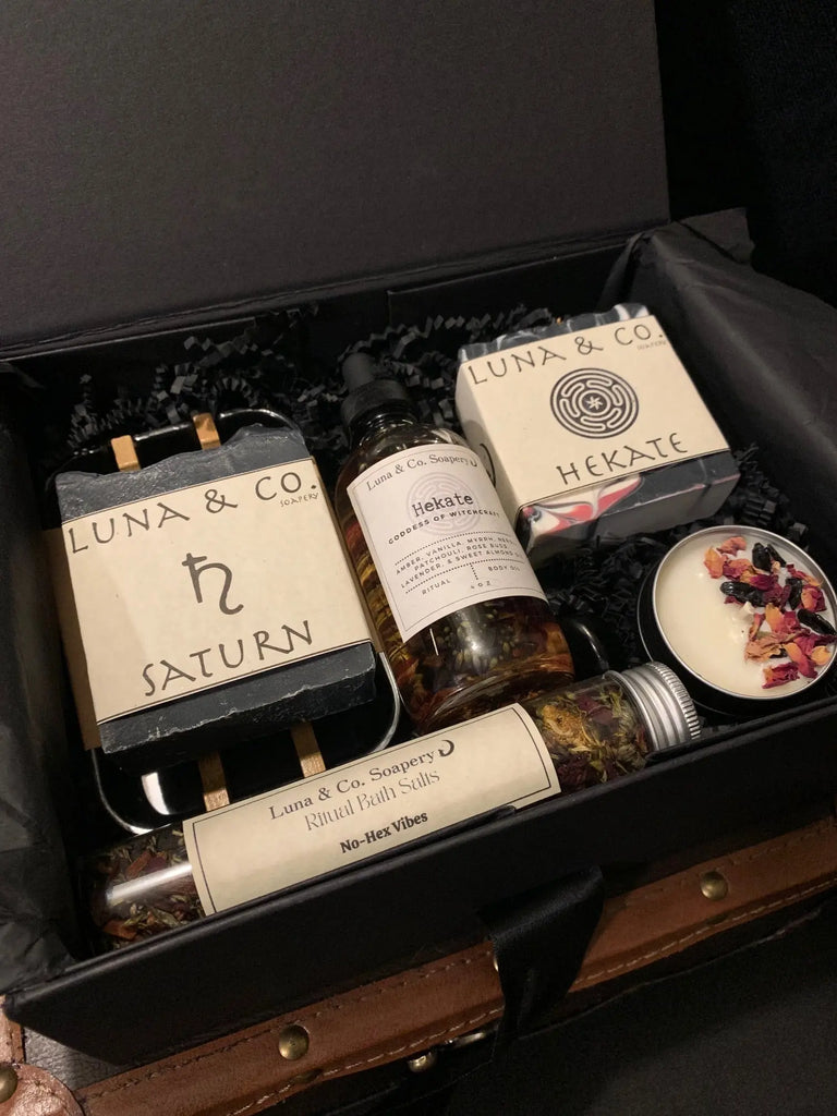 The Celestial Gift Set by Luna & Co. Soapery features a black gift box with artisanal Goddess Soaps (Saturn & Hekate), ritual bath salts, spray bottle, and candle tin with dried flowers—a truly celestial collection of bath treats.