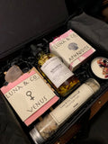 The Celestial Gift Set by Luna & Co. Soapery includes Venus and Aphrodite soaps, floral bath oil, a dried petal candle, soothing bath salts, and a crystal—all nestled in black shredded paper.