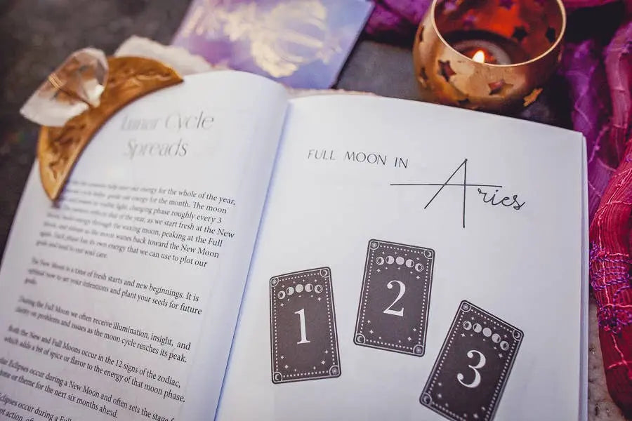 The Cosmic Guidance Book by Bella deLuna is open to a Full Moon in Aries tarot spread. Surrounded by a lit candle and crystals, it offers a mystical setting for self-discovery through astrology and tarot.