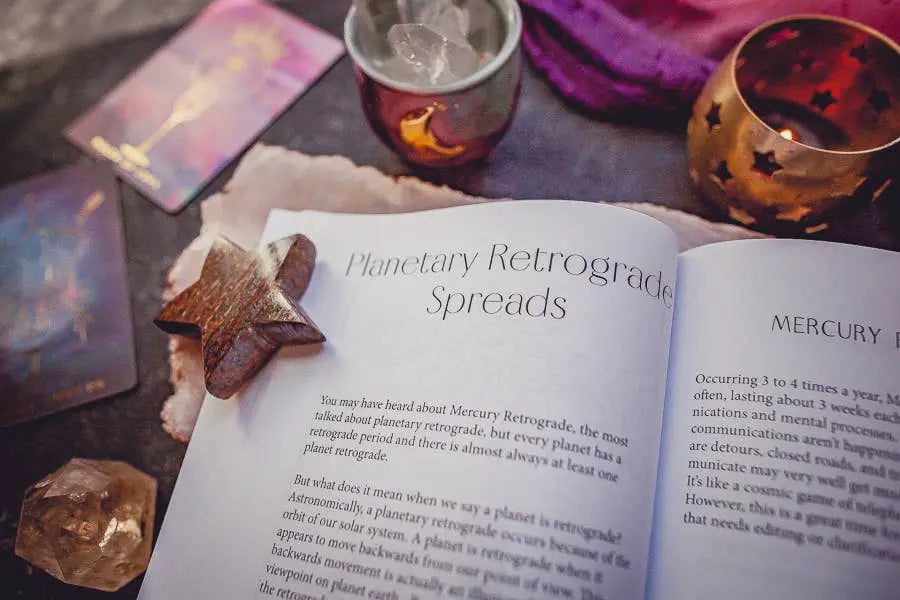 The Cosmic Guidance Book by Bella deLuna lies open to Planetary Retrograde Spreads, surrounded by tarot cards, crystals, a wooden star, and candles—an inspiring celestial roadmap for astrology lovers.