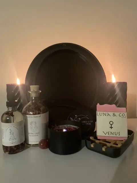 Create a stunning ritual with the Divine Love Ritual Kit by Luna & Co. Soapery, featuring two black candles, black plate, “Divine Love” bottles, the VENUS bar, incense sticks, red stone, and black bowl—ideal for self-love ceremonies.