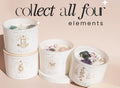 The Air Elements Candle 12oz by THE MINDFUL COLLECTIVE is displayed on a beige background with stylish black text: “Collect all four elements.” Perfect as a Zodiac Candle or Air Signs Candle set.