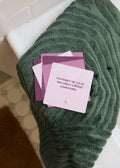A stack of JaxKelly Shower Affirmation™ Cards - Boundaries rests on a textured green towel, with the top card stating, “I no longer say yes so that others will feel comfortable.” White tile and a brown mat are in the background.