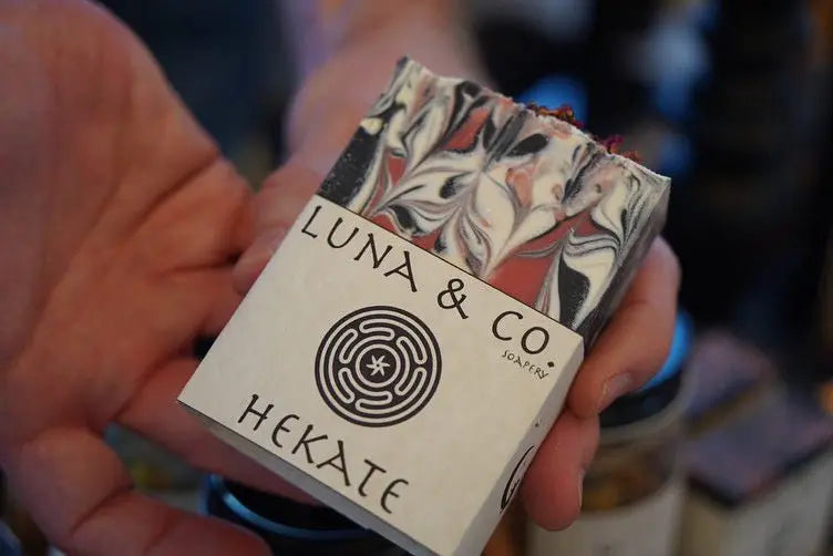 A hand holds a bar of Luna & Co. Soapery’s Hekate: Goddess of Witchcraft soap, featuring a striking black, white, and red marbled pattern—ideal for rituals or daily self-care.