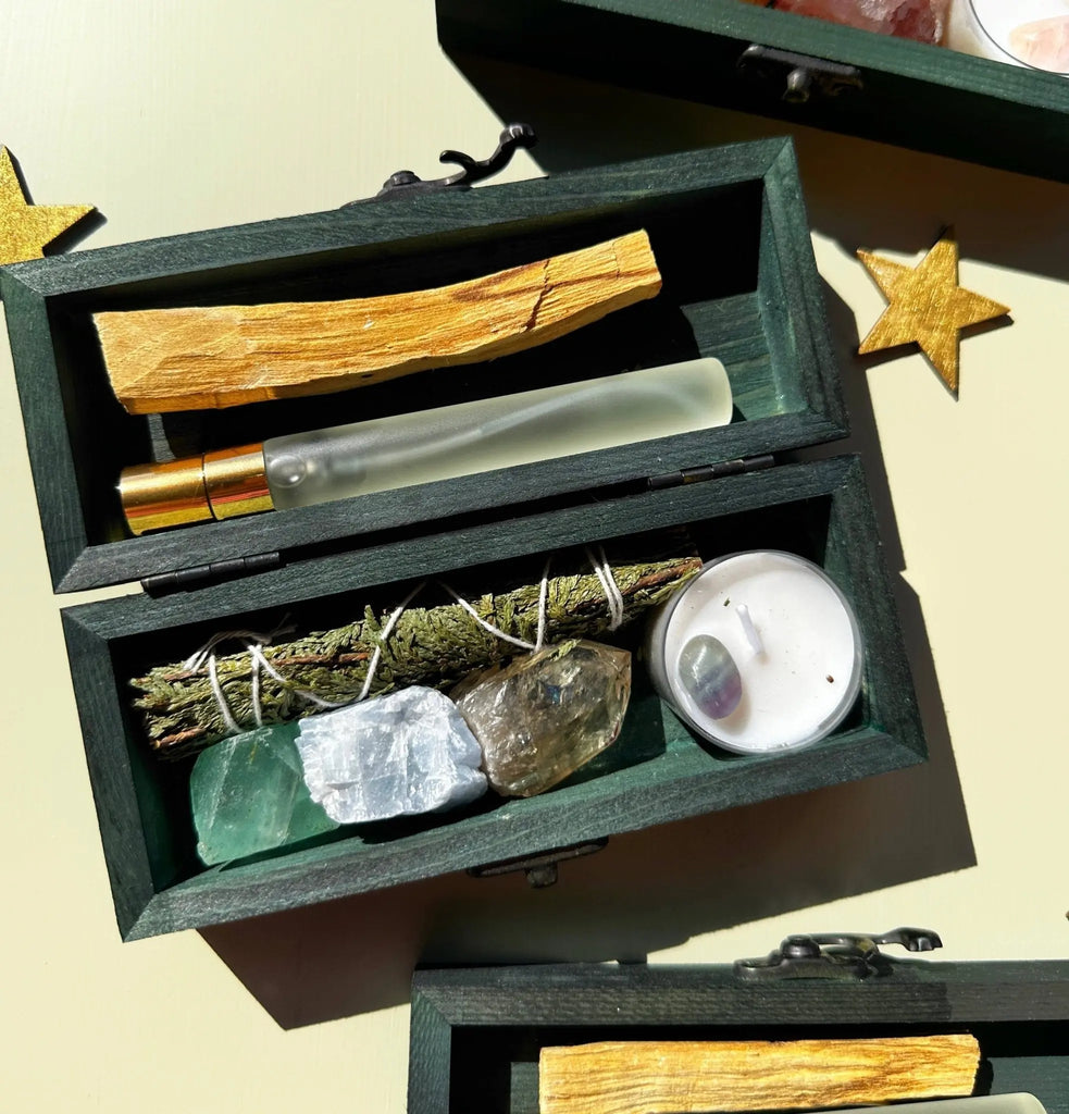 The 12th Moon PROTECTING MY ENERGY KIT includes a stick of wood, glass roller bottle, dried herbs, stress relief crystals, and tealight candle. Two wooden stars rest nearby, making this INTENTIONS KIT perfect to dream and manifest positive energy.