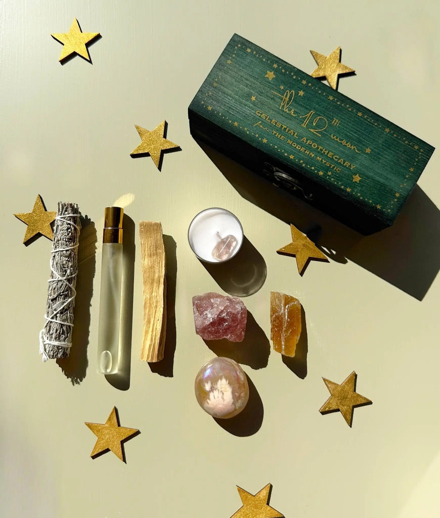 A flat lay of The 12th Moon PROTECTING MY ENERGY KIT features sage, palo santo, a perfume roller, candle with crystal, rose quartz, and more—an ideal crystal kit to relieve stress and remove negativity.