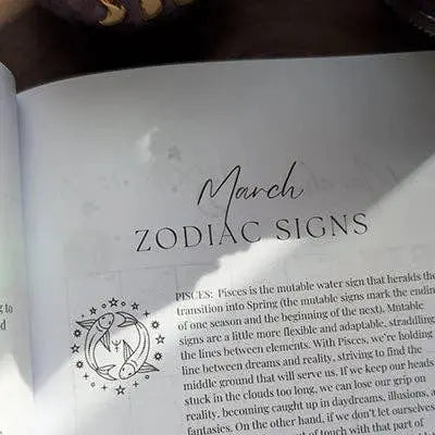 A page from the Bella deLuna Soul Care Moon Journal features a decorative Pisces symbol and insights about Pisces traits tied to moon cycle rituals, with sunlight partially illuminating the journal.