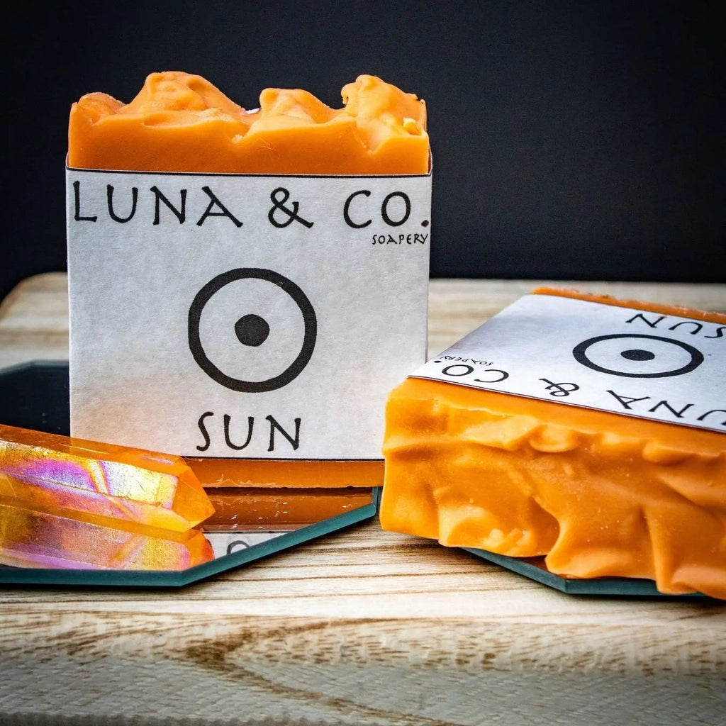 Frankincense, Juniper and Orange essential oil. Handcrafted Sun Soap bar, golden-yellow with mica, infused with juniper, frankincense, and orange oils, on a wooden dish.